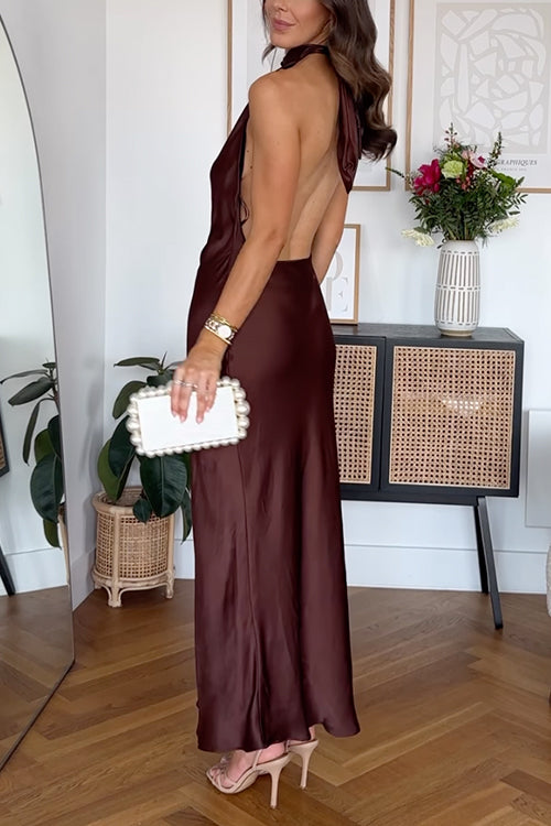 Woman wearing a long, dark brown satin dress with a halter neckline and an open back, holding a white pearl-embellished clutch.