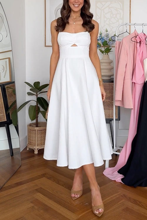 Woman wearing a white midi dress with a sweetheart neckline and a cut-out detail. She is also wearing tan heels and holding a woven handbag.