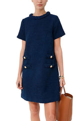A woman wearing a navy blue tweed shift dress with short sleeves and decorative pockets, holding a brown leather tote bag.