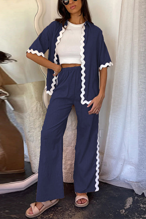 Woman wearing a navy blue linen-like pajama set with white scalloped trim, paired with a white crop top and beige sandals.