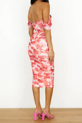 back view of a woman in a pink and red floral print off-the-shoulder ruched midi dress and pink strappy heels