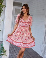 Woman wearing a pink floral print mini dress with puff sleeves and a tie neck