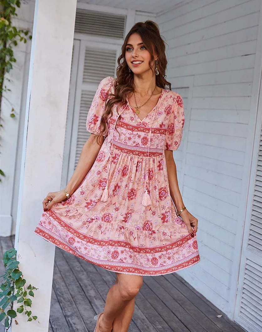 Woman wearing a pink floral print mini dress with puff sleeves and a tie neck