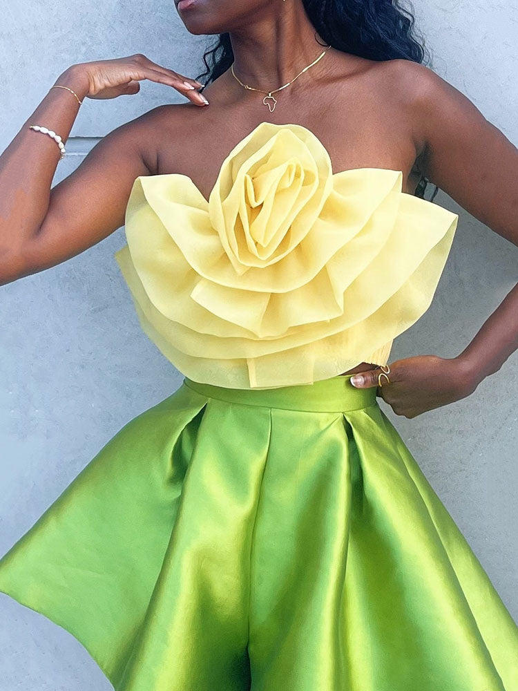 A woman in a yellow floral strapless top and green pleated shorts.