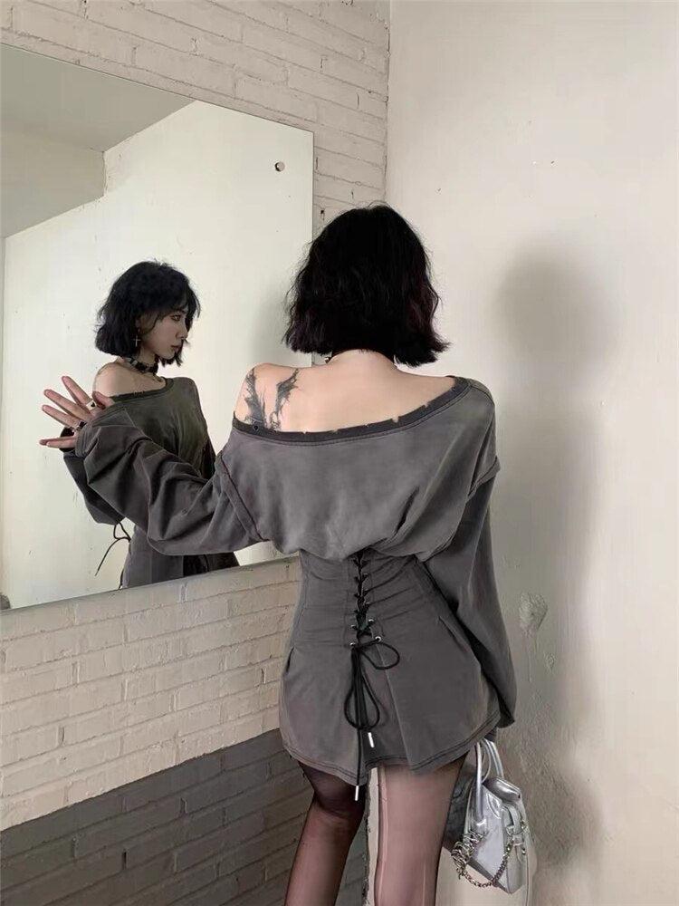 Woman in a mirror reflection wearing a gray off-the-shoulder dress with a lace-up corset waist and distressed details.