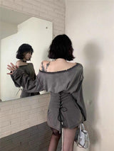 Woman in a mirror reflection wearing a gray off-the-shoulder dress with a lace-up corset waist and distressed details.