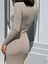 A woman with dark bob haircut poses from the back in a beige ribbed knit maxi dress, leaning against a white structure.
