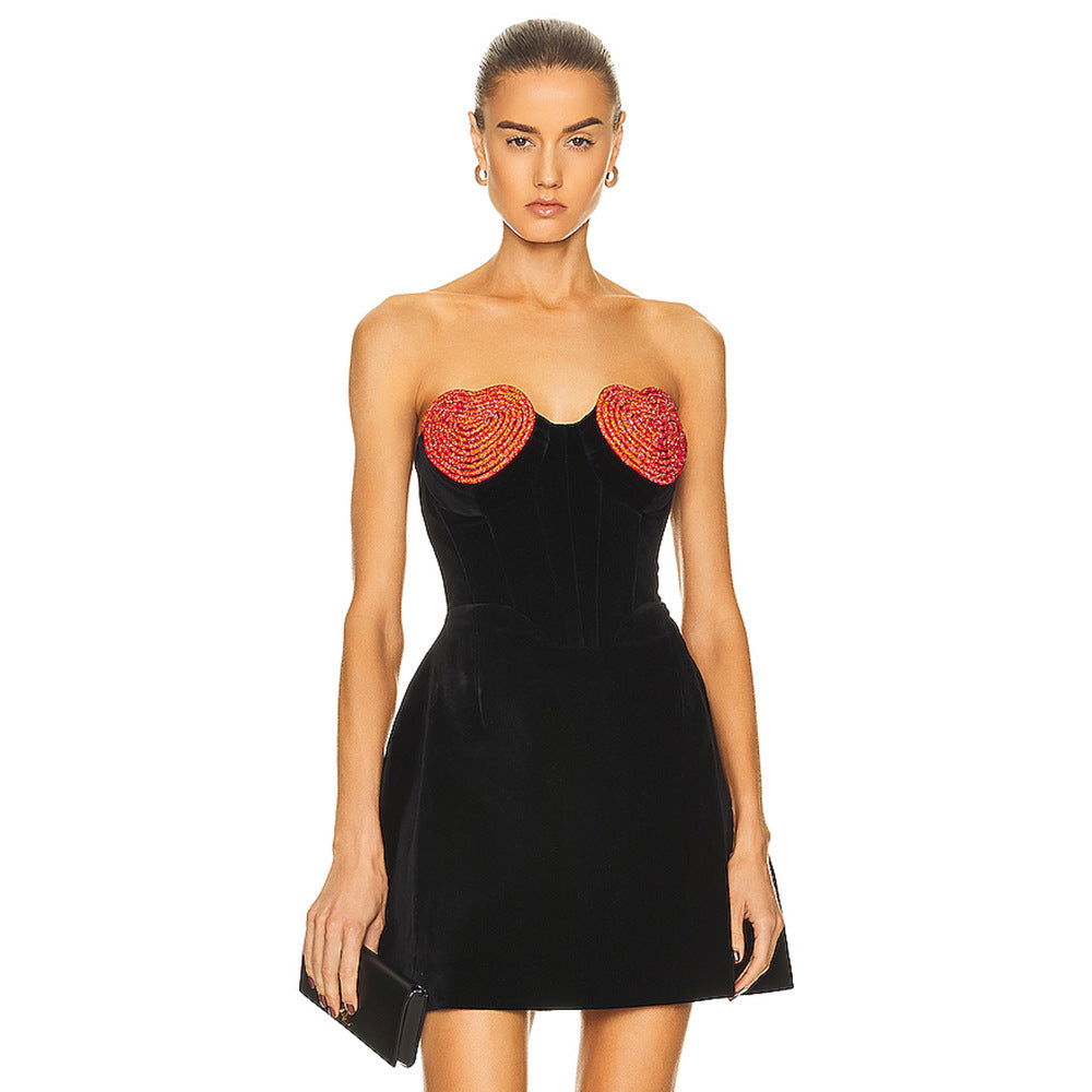 A model wearing a black strapless dress with red heart embellishments, holding a black clutch.