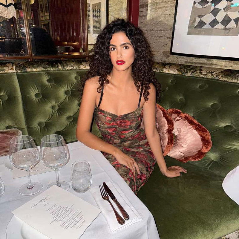 Woman with curly hair sitting on a green velvet couch wearing a floral print ruched dress