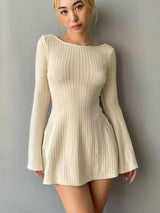 A woman stands facing forward, wearing a cream knit mini dress with long bell sleeves and a scoop neckline.