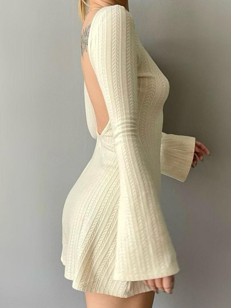 Side view of a woman in a cream knit mini dress, showing the open back and bell sleeves.
