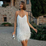 Woman in a white sequined and feathered mini dress with spaghetti straps, holding a white clutch and smiling.