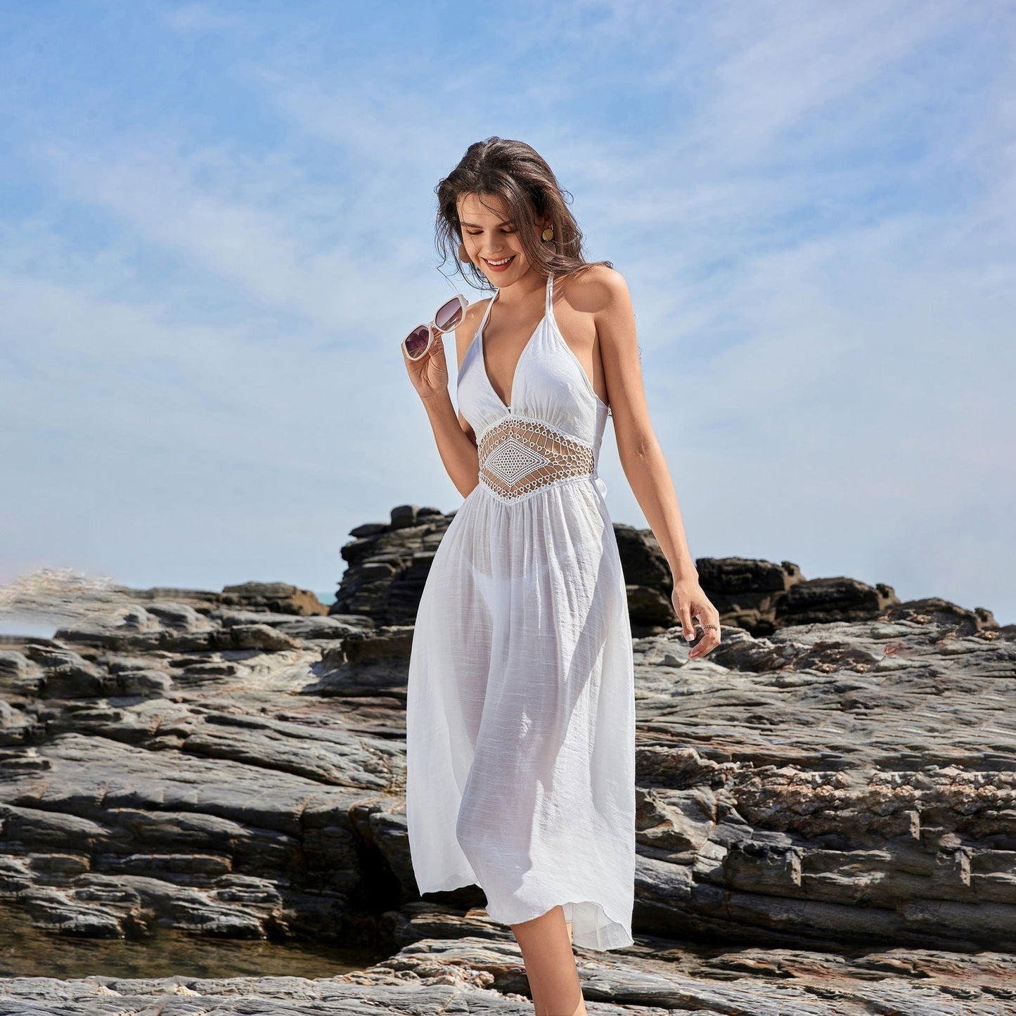Woman in a white halter neck dress walking on rocks by the sea
