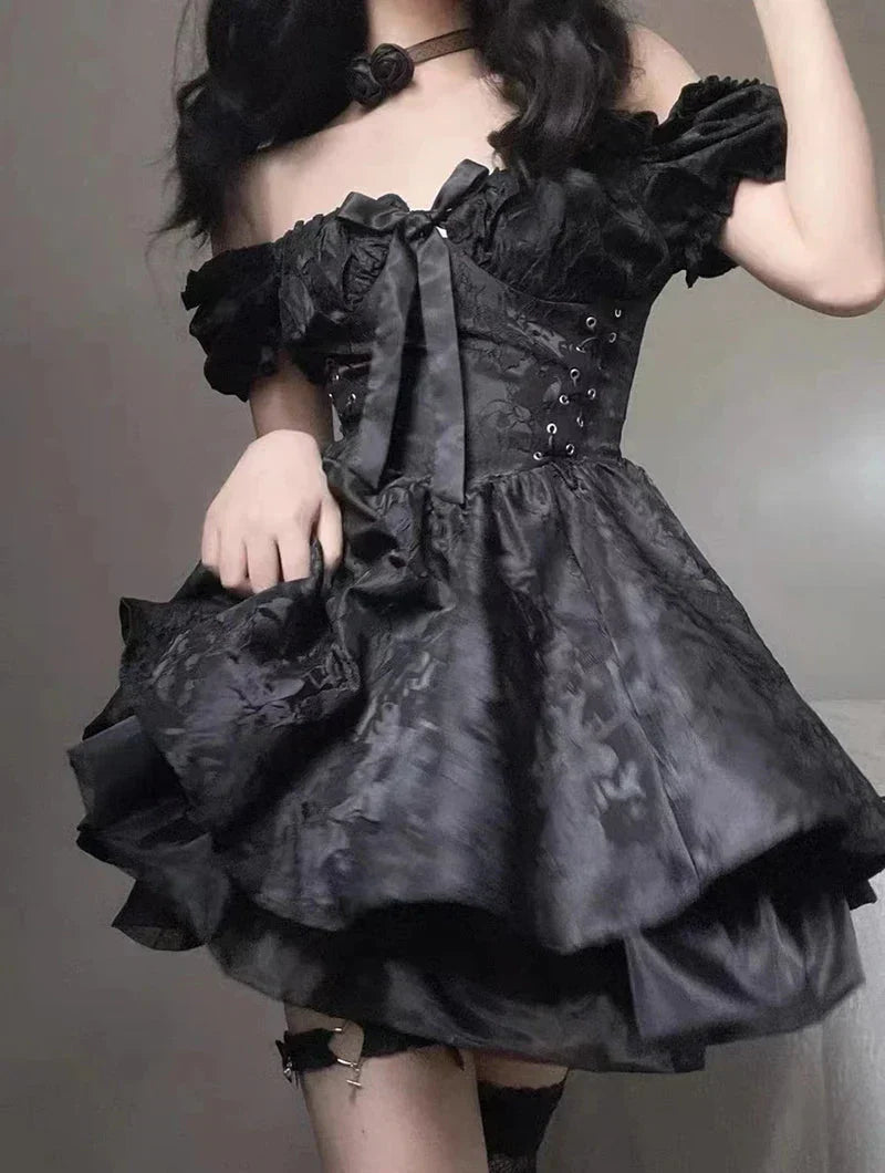 Woman in a black off-the-shoulder dress with corset detailing and a tiered skirt, holding the skirt.