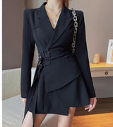 A woman poses in a black blazer dress with a wrap skirt and belted waist.