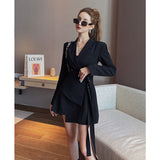 A woman in a black blazer dress with sunglasses and a black handbag.