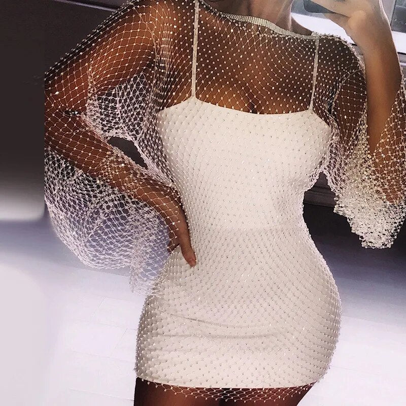 A woman wearing a white slip dress with a sheer, sparkling white mesh overlay with bell sleeves.