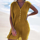 A woman wearing a mustard yellow sleeveless dress with a v-neck and button-down front, standing on a beach.