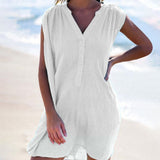 A woman wearing a white sleeveless dress with a v-neck and button-down front, standing on a beach.