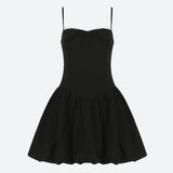 A black spaghetti strap dress with a white lace trim and a bow detail, laid flat.