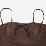 Close-up of the bustier top of a brown spaghetti strap dress with a black bow and lace trim.