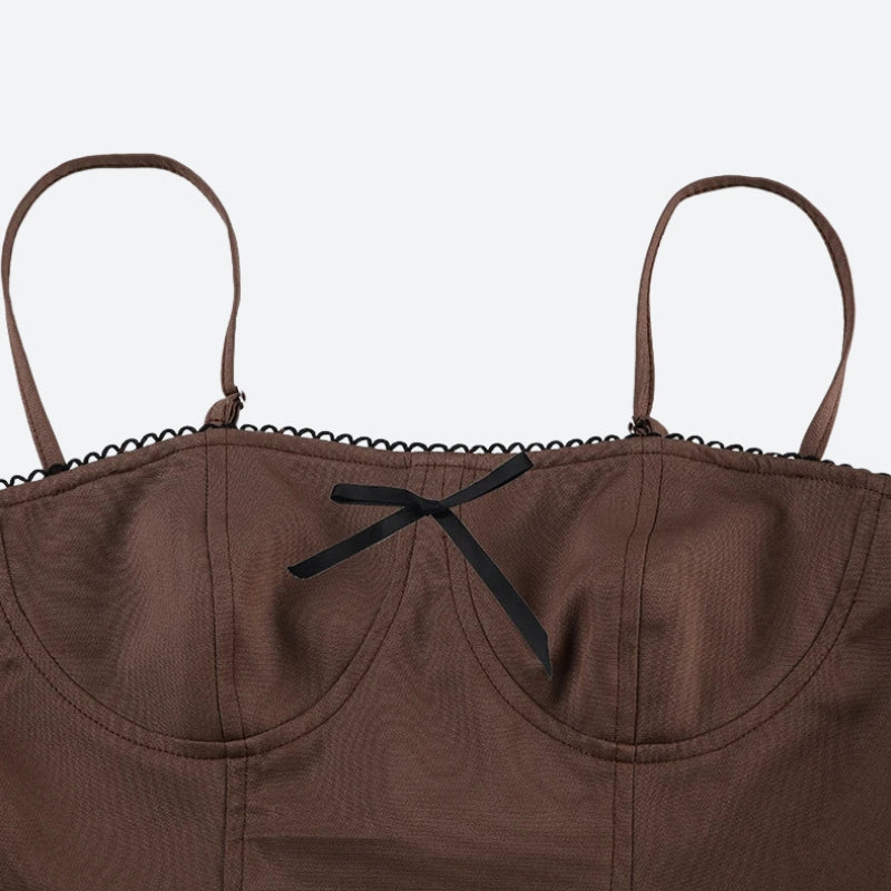 Close-up of the bustier top of a brown spaghetti strap dress with a black bow and lace trim.