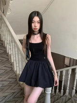 A woman wearing a black tank top and a black mini skirt stands on a staircase.