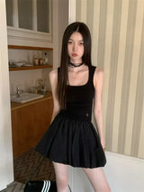 A woman wearing a black tank top and a black mini skirt stands in a room with striped wallpaper.