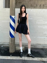 A woman wearing a black tank top and a black mini skirt stands next to a striped pole.