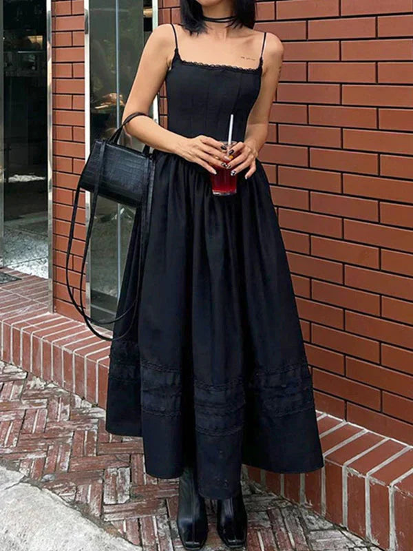 Woman in a black midi dress with lace trim, holding a red drink and a black handbag.