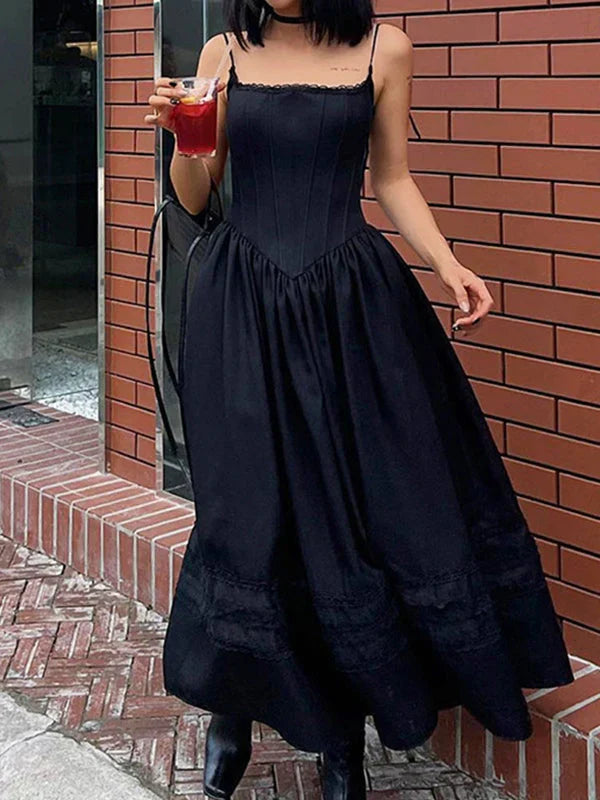 Woman wearing a black midi dress with spaghetti straps and a full skirt, holding a red drink.