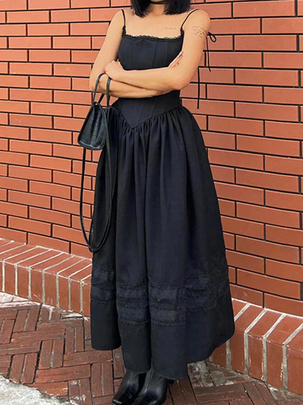 Woman with arms crossed, wearing a black midi dress and black boots, standing against a brick wall.