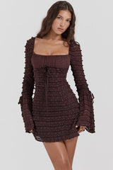 Woman wearing a short, brown, long-sleeved ruched dress with a square neckline and bell sleeves.