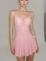 A young woman wearing a pink slip dress with lace detailing on the bust and a pleated skirt.
