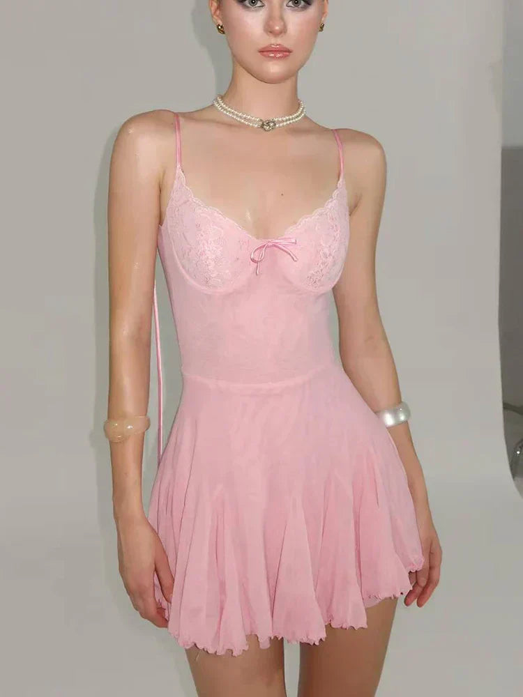 A young woman wearing a pink slip dress with lace detailing on the bust and a pleated skirt.