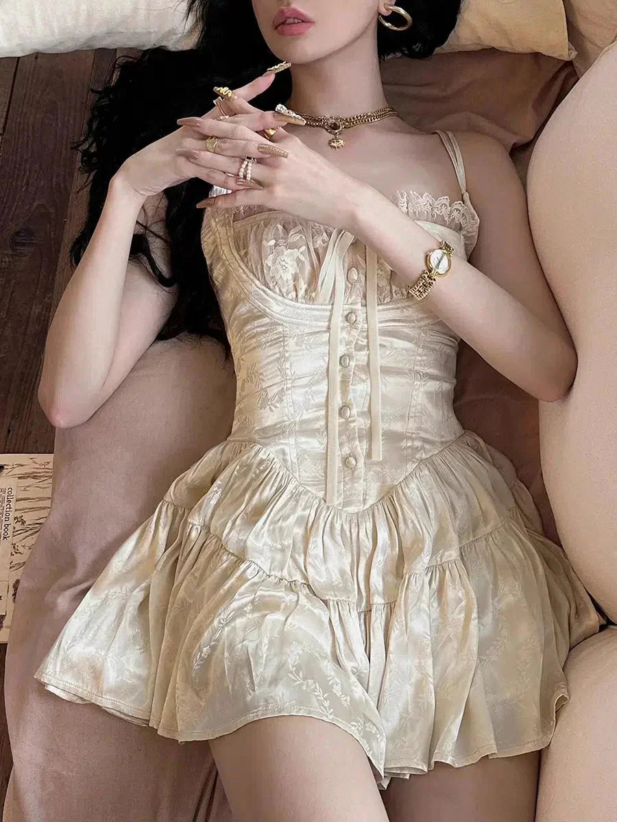 A woman lying down wearing a cream corset-style mini dress with lace trim and a tie front, with her hands resting on her chest.