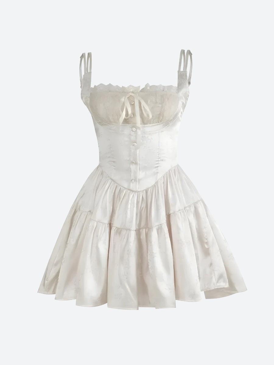 A white corset-style mini dress with spaghetti straps, lace trim, a tie front, button detailing, and a ruffled tiered skirt, shown against a white background.