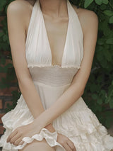 A woman in a white ruffled dress sits with her arms crossed.