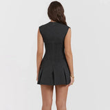 The back of a woman wearing a dark gray sleeveless mini dress with a plunging V-neck and a pleated skirt.