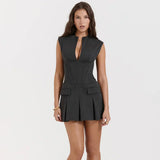 A woman wearing a dark gray sleeveless mini dress with a plunging V-neck and a pleated skirt.