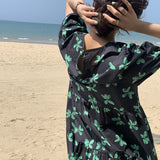 Close-up of the back of a woman wearing a black dress with a green floral print and a cutout detail.