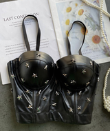 A black leather bustier top adorned with silver star studs, laid flat on top of an open book with a floral print.