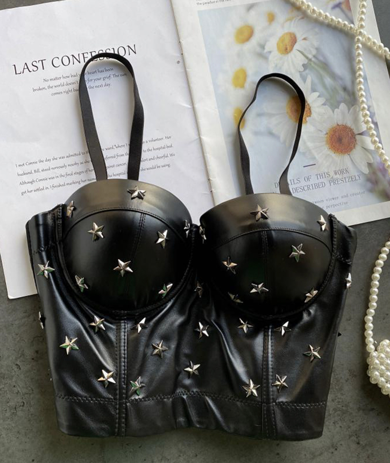 A black leather bustier top adorned with silver star studs, laid flat on top of an open book with a floral print.