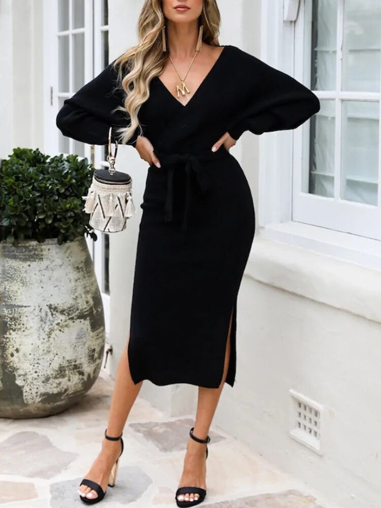 woman wearing a black knitted wrap dress with a belted waist and batwing sleeves, accessorized with a handbag and heels