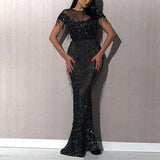 Woman in a black sequined mermaid gown with sheer illusion neckline and tassel details