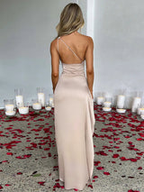 Woman in a beige one-shoulder satin gown with a high slit, seen from the back.