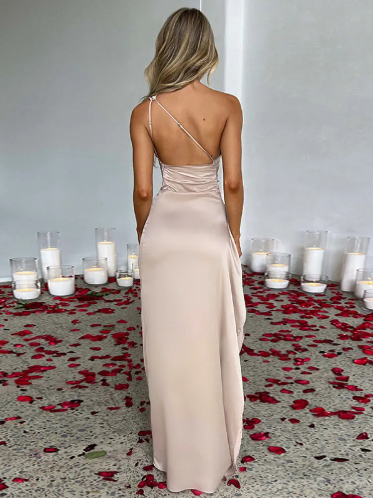 Woman in a beige one-shoulder satin gown with a high slit, seen from the back.