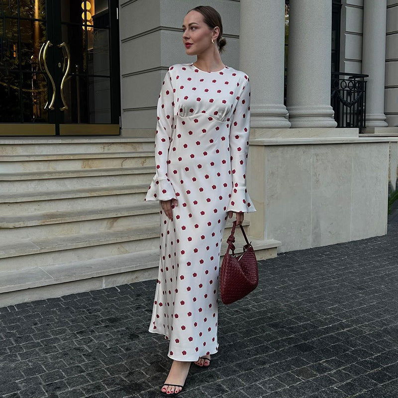 Woman wearing a white polka dot maxi dress with red polka dots and bell sleeves, holding a red bag.