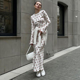 Woman wearing a white polka dot maxi dress with red polka dots and bell sleeves, with white sneakers and a white sweater tied around her waist.