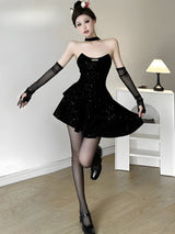 Woman posing in a black sequined strapless dress, black tights, and black heeled shoes, with sheer opera gloves.